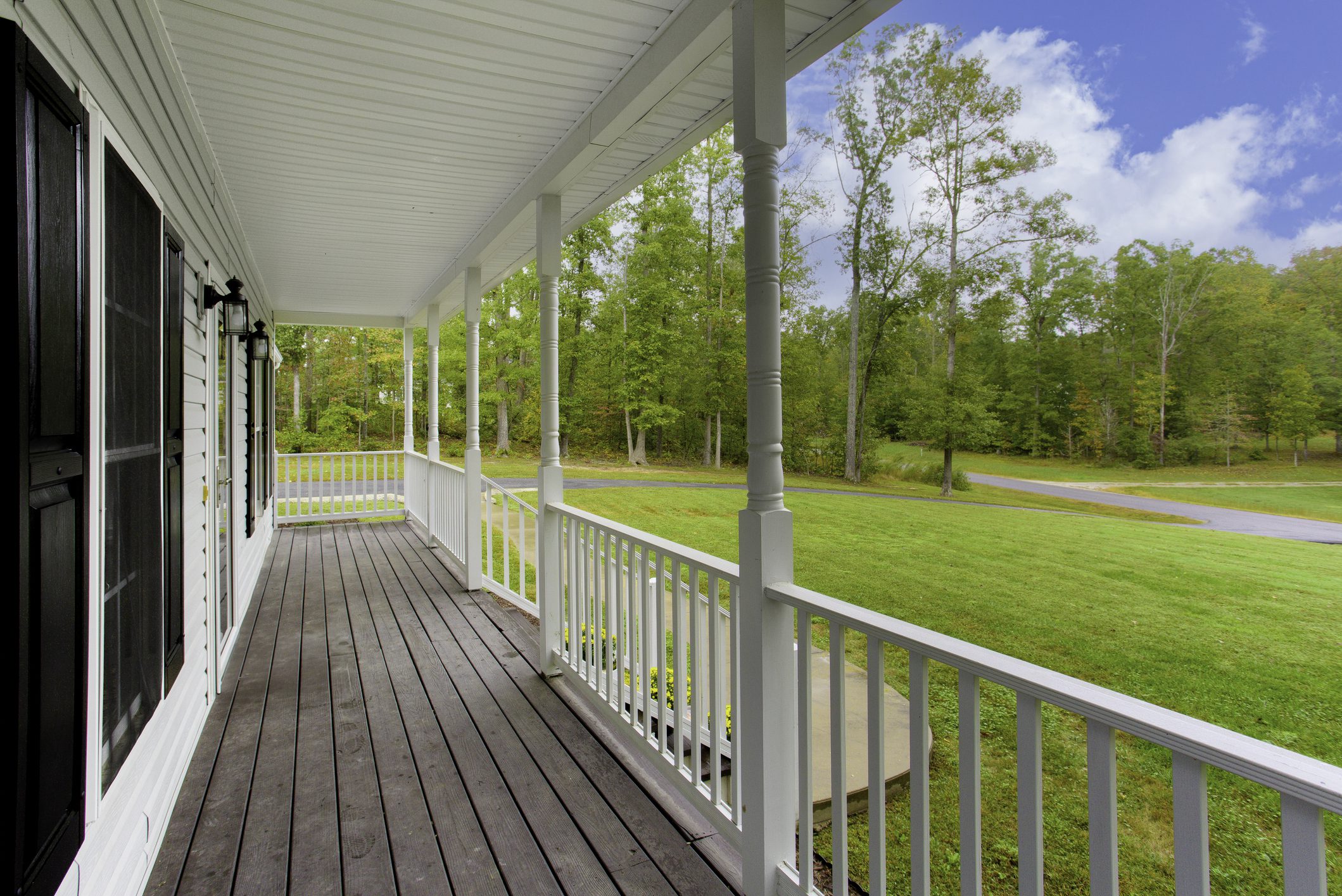 A serene white-covered porch with classic railing, providing a perfect spot to enjoy the surrounding lush greenery and clear blue sky, creating a peaceful and inviting setting.