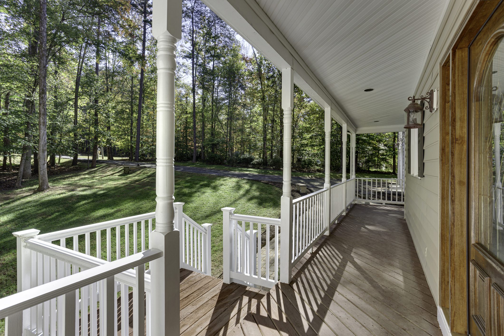A charming covered porch features classic white railings and overlooks a beautifully wooded area, offering a tranquil retreat to enjoy the surrounding natural landscape.